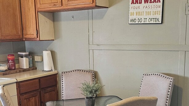 Une cuisine avec des meubles en bois, une table à manger avec quatre chaises et une citation inspirante sur le mur.