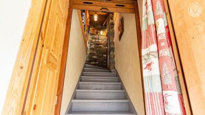 Eine Holztreppe führt zu einem Raum mit Steinwänden und einer hängenden Leuchte.