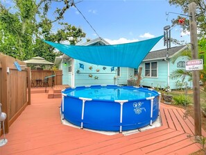 Ein blauer Aufstellpool mit Holzterrasse, umgeben von einem Holzzaun und einem Haus mit einem Schild mit der Aufschrift 'Beware of Shark'.