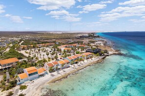 Luftaufnahme eines Küstenresorts mit mehreren Gebäuden, einem Strandabschnitt und klarem, blauem Wasser.