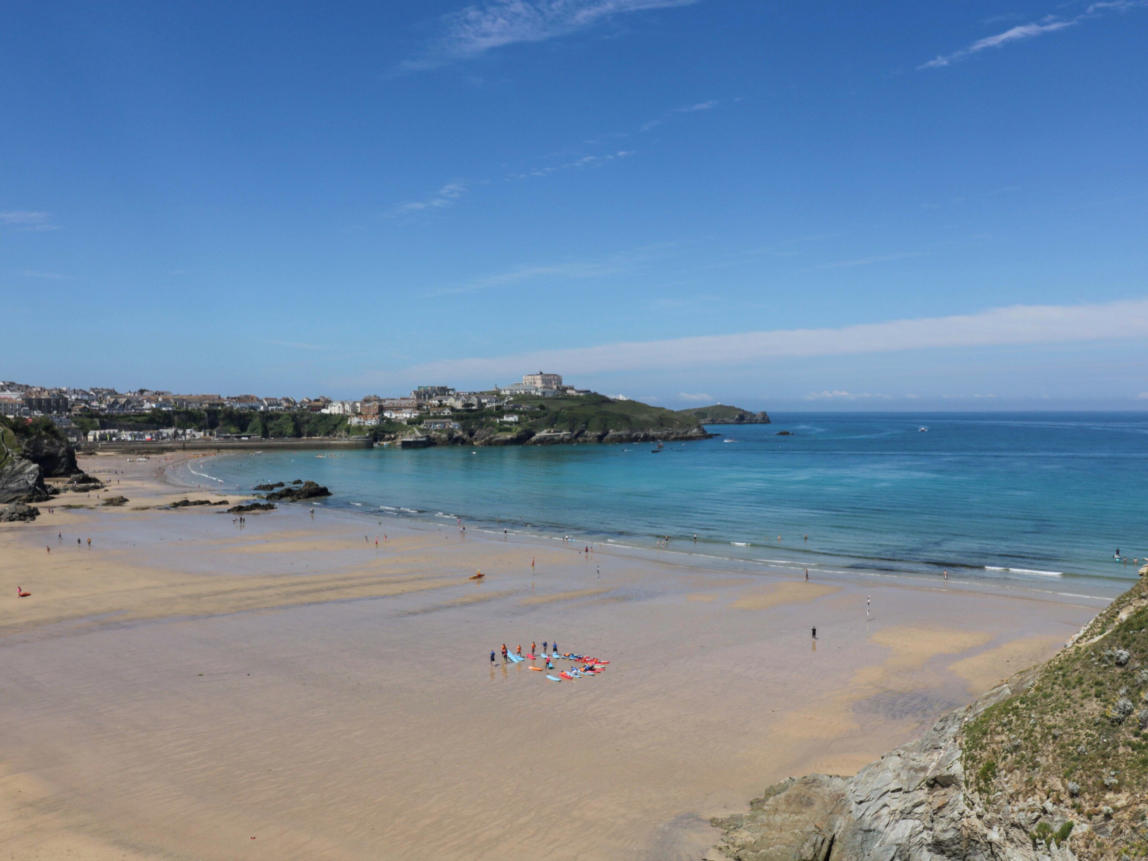 Uma praia costeira com céu claro, faixa de areia e edifícios ao fundo.
