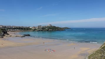 Uma praia costeira com céu claro, faixa de areia e edifícios ao fundo.