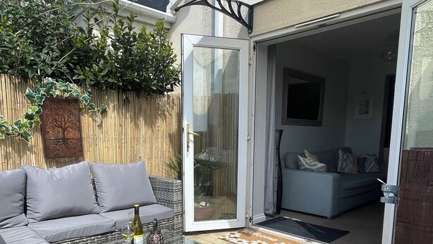 An outdoor seating area with a sofa, a glass table, and a bottle of wine. - Tolcarne Reach (Newquay)