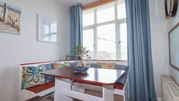 Uma área de refeições com bancos, uma mesa, um vaso de planta e uma janela com cortinas.