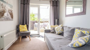 A living room with a grey sofa, yellow patterned pillows, a grey armchair, a radiator, and a painting on the wall. - Tolcarne Reach (Newquay)