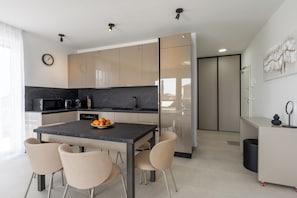 A modern kitchen with a marble countertop, a dining table with chairs, and a clock on the wall. - Apartment Apartman Carolina (Istria - Novigrad) (Novigrad)