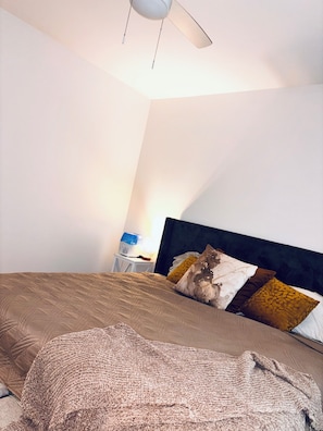 Ein Schlafzimmer mit Bett, Nachttisch, Lampe und Deckenventilator.
