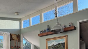 A dining area with a wooden table and chairs, a ceiling fan, a painting, and a window with a view of trees. - Cozy Lake Cottage in charming Dunstable (Dunstable)