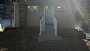 A house with a stone chimney, a light blue door, and a small porch. - Cozy Lake Cottage in charming Dunstable (Dunstable)