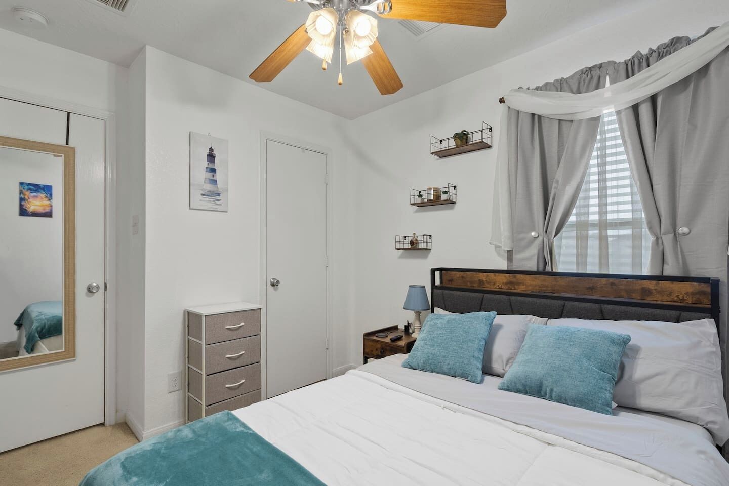 A bedroom with a bed, a ceiling fan, a nightstand, a mirror, a wardrobe, and a window with curtains.