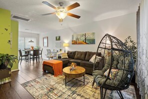 Sala de estar com ventilador de teto, sofá, mesa de centro, área de refeições e cadeira suspensa.