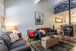 A modern living room with a fireplace, grey sofas, and a large wall-mounted deer artwork. - Centrally Located Townhouse - Jacuzzi & Parking! (Mammoth Lakes)