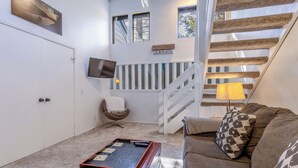 A room with a sofa, a red table, a chair, a TV, a staircase, and a window. - Centrally Located Townhouse - Jacuzzi & Parking! (Mammoth Lakes)