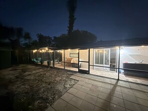 Ein modernes Haus mit einer verglasten Terrasse, Sitzmöglichkeiten im Freien und einem Poolbereich.