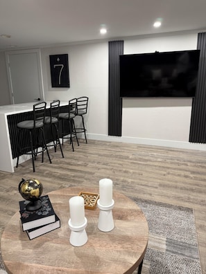 Ein modernes Wohnzimmer mit einem runden Holztisch, einem schwarzen und goldenen Globus, zwei weißen Kerzen und einem Bücherregal.