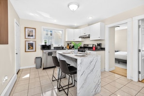 A modern kitchen with white cabinets, a marble island, and bar stools. - Huge Home Near Downtown Boston! Bow Market, Harvard, MIT, Union Square! (Somerville)