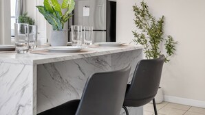 Eine moderne Küche mit Marmorarbeitsplatten, schwarzen Stühlen und einem Blumentopf.