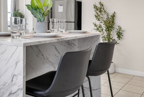 Eine moderne Küche mit Marmorarbeitsplatten, schwarzen Stühlen und einem Blumentopf.