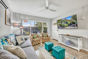 A modern living room with a grey sofa, patterned armchairs, a teal ottoman, a white console table, and a large TV on the wall. - 🌴 Beachside Bungalow | Entire Duplex, Walk to Crescent Beach, 2 Hot Tubs and Community Pool (Siesta Key)