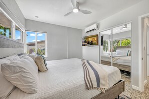 Une chambre à coucher avec un lit, un ventilateur de plafond, une grande fenêtre et une vue sur l’extérieur.