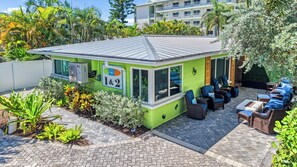 A green building with a tiled roof, outdoor seating area with wicker furniture, and a sign indicating '1&2' on the side. - 🌴 Crabby Bungalow | Duplex Unit, Walk to Crescent Beach, & Hot Tub (Siesta Key)