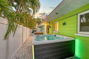 A spa area with a hot tub, a white fence, and a green building. - 🌴 Crabby Bungalow | Duplex Unit, Walk to Crescent Beach, & Hot Tub (Siesta Key)