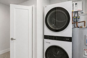 A laundry room with stacked washers and dryers, a white door, and visible plumbing. - 🌴 Crabby Bungalow | Duplex Unit, Walk to Crescent Beach, & Hot Tub (Siesta Key)