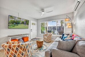 A living room with a television, sofa, armchair, and a ceiling fan. - 🌴 Crabby Bungalow | Duplex Unit, Walk to Crescent Beach, & Hot Tub (Siesta Key)