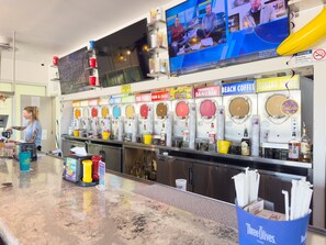 A bar area with a variety of drink dispensers, a television screen, and a counter with a person working. - 🌴 Crabby Bungalow | Duplex Unit, Walk to Crescent Beach, & Hot Tub (Siesta Key)