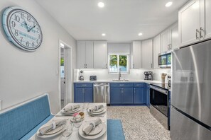 A modern kitchen with blue cabinets, a stainless steel refrigerator, and a clock on the wall. - Sea Turtle Bungalow | Private Unit in Duplex, Walk to Crescent Beach & Community Pool (Siesta Key)