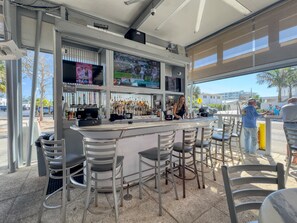 A bar area with a counter, multiple seating options, and a large screen displaying sports. - Sea Turtle Bungalow | Private Unit in Duplex, Walk to Crescent Beach & Community Pool (Siesta Key)