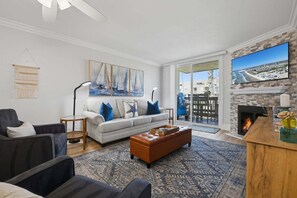 Ein Wohnzimmer mit einer Couch, Sesseln, einem Couchtisch, einem Kamin und einem großen Fernseher.