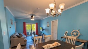 Un coin repas avec une table en bois, des chaises blanches, un lustre et une décoration en forme de roue de voilier.
