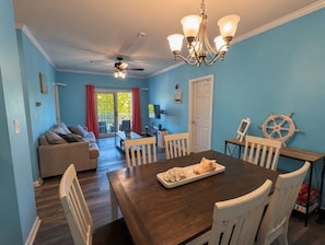 A dining area with a wooden table, white chairs, a chandelier, and a sail wheel decoration. - Dog-Friendly 2BR/2BA Condo Near Rehoboth Beach (Rehoboth Beach)