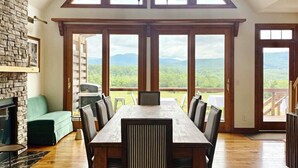 A dining area with a high ceiling, large windows, and a view of the outdoors.