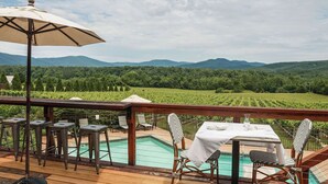 A deck with a pool, outdoor seating, and a view of a vineyard.