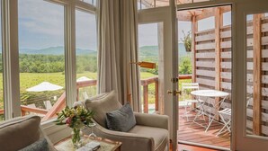 A room with a sofa, a small table with a vase, and a view of a lush landscape through large windows.