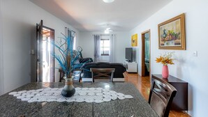 A modern living room with a dining area, a sofa, a TV, and a painting on the wall. - Casa com Churrasqueira e Rede a 210 m da Praia (Navegantes)