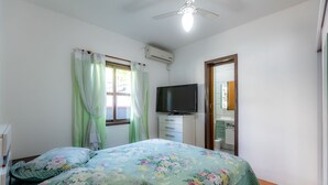 A bedroom with a bed, curtains, a television, a mirror, and an air conditioning unit. - Casa com Churrasqueira e Rede a 210 m da Praia (Navegantes)