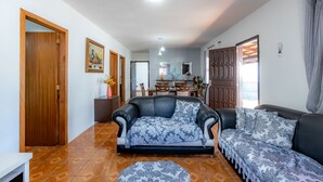 A living room with a sofa, a coffee table, a dining area with chairs, and a ceiling fan. - Casa com Churrasqueira e Rede a 210 m da Praia (Navegantes)