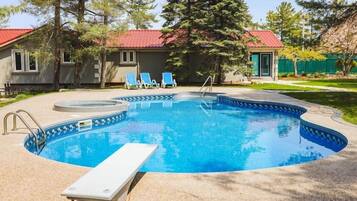 A swimming pool with a hot tub, lounge chairs, and a small building with a red roof.