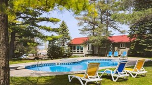 A swimming pool with lounge chairs, surrounded by trees and a building with a red roof.