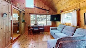A wooden cabin interior with a dining table, sofa, and TV.