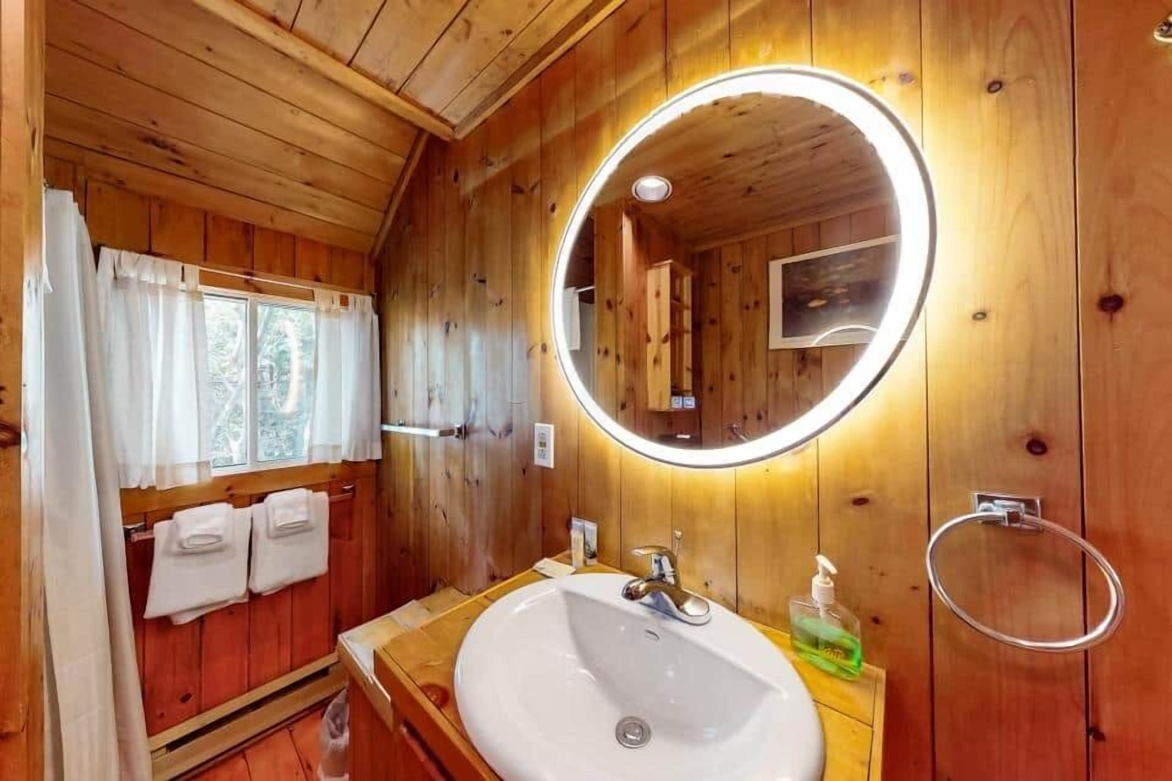Une salle de bain rustique, avec des murs en bois, un miroir rond, un lavabo blanc et un porte-serviettes.