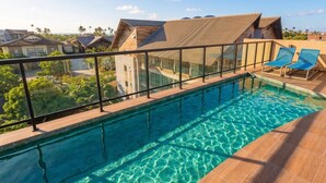 En swimmingpool med gelænder af glas, to blå liggestole og udsigt til omkringliggende bygninger.