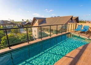 Ein Swimmingpool mit Glasgeländer, zwei blaue Liegestühle und Blick auf umliegende Gebäude.