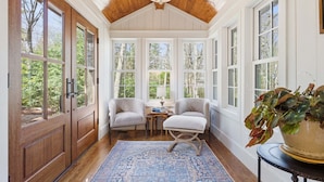 A sunroom with large windows, wooden ceiling, two chairs, a small table, and a blue rug. - Sunset Nest, Walk to Town (Highlands)