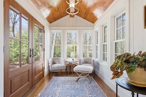 A sunroom with large windows, wooden ceiling, two chairs, a small table, and a blue rug. - Aschmeyer's, Walk to Town (Highlands)