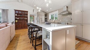 A kitchen with a central island, bar stools, wooden cabinets, and pendant lighting. - Sunset Nest, Walk to Town (Highlands)