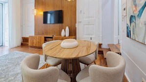 Uma sala de estar moderna com uma mesa redonda de madeira, duas cadeiras, uma TV de tela plana fixada em uma parede de madeira e um quadro na parede.